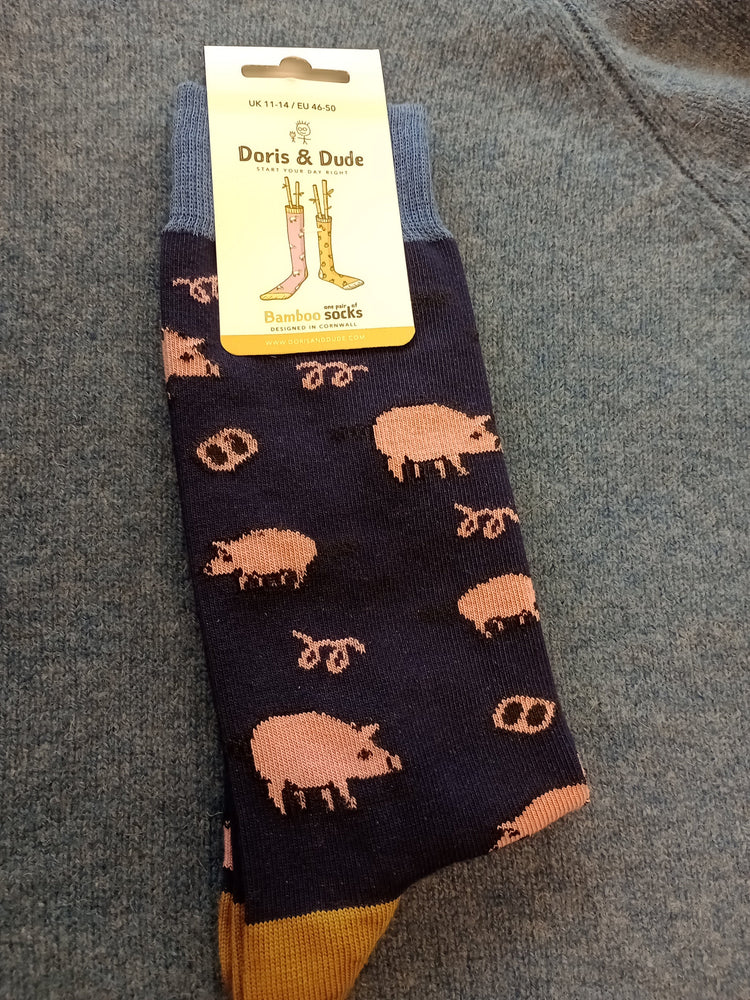 A pair of dark navy crew socks with a pinkish-brown pig pattern and mustard yellow heels, shown with a yellow 'Doris & Dude' brand tag.